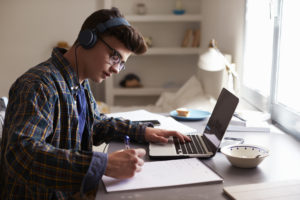十幾歲的男孩，戴著耳機在他的臥室的辦公桌前工作