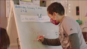 сурагч цагаан самбар дээр бичдэг