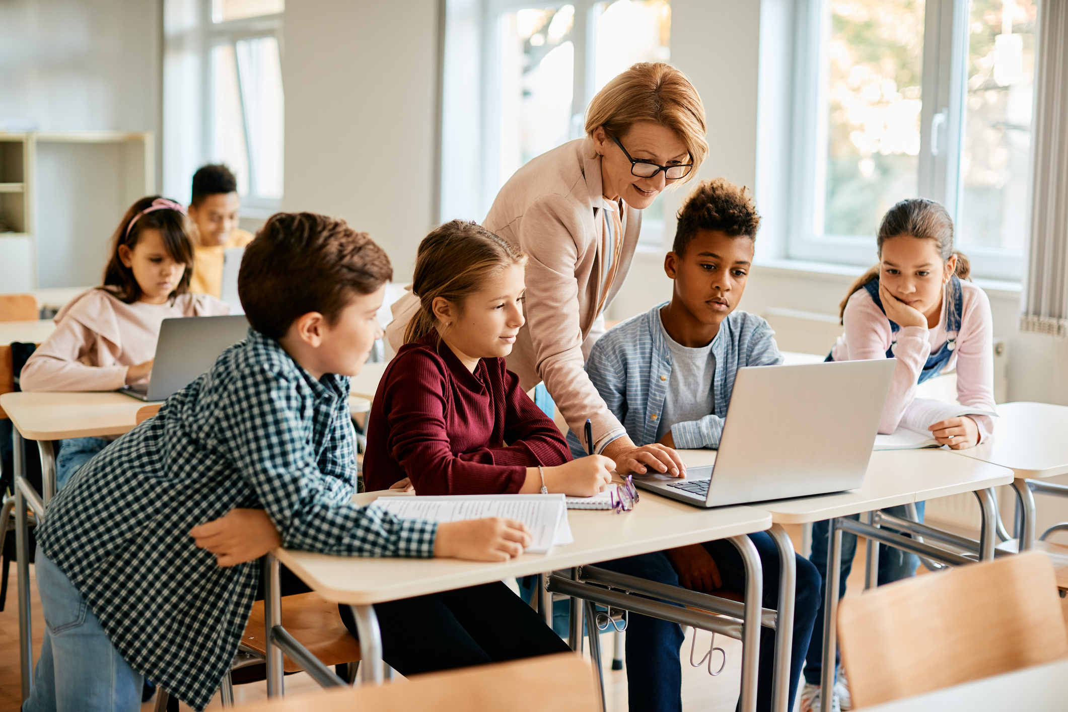 Grupo de alunos do ensino fundamental tendo aula de informática com seu professor na sala de aula.