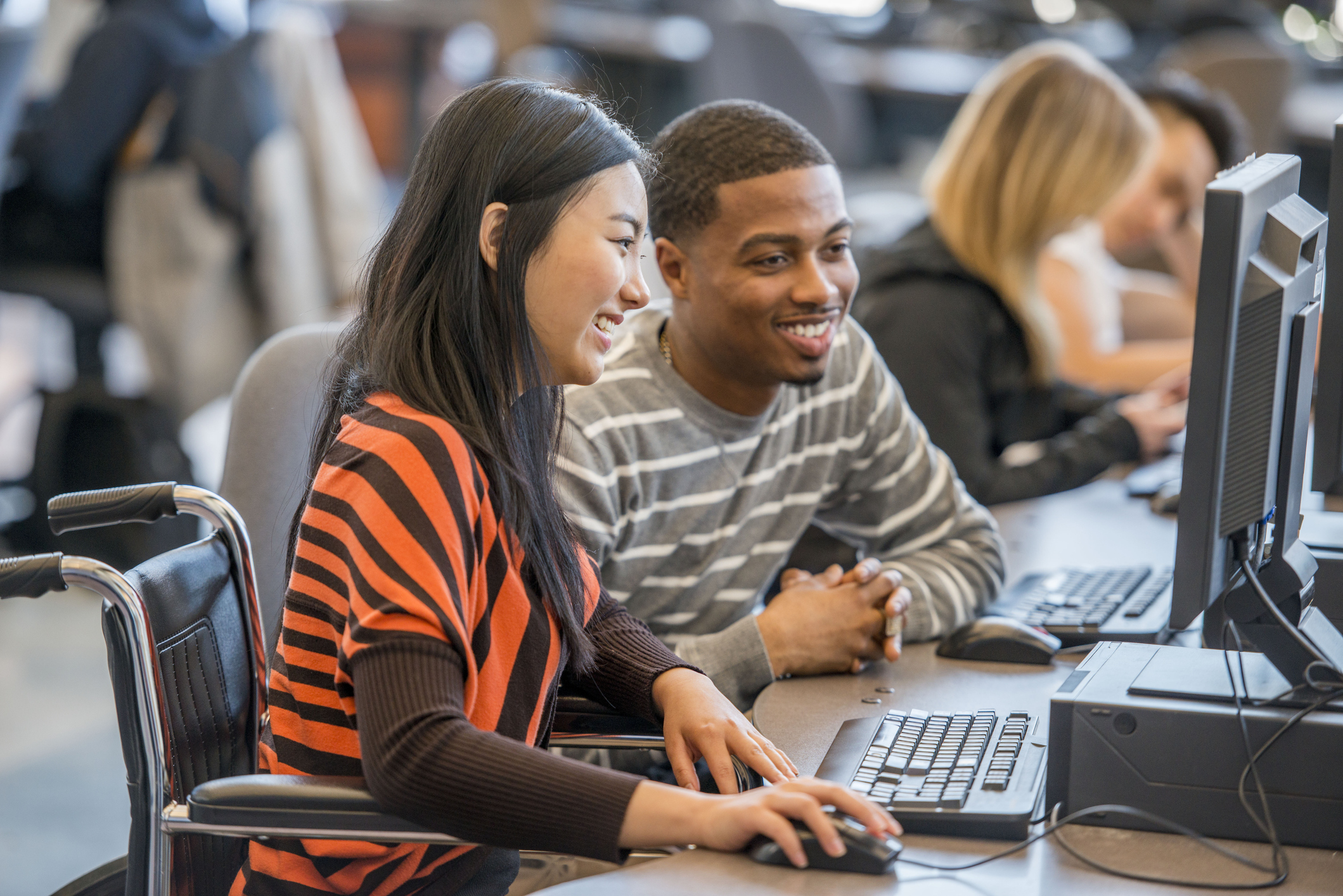 A multi-ethnic group of college age students are working on computers in the lab during a university class.