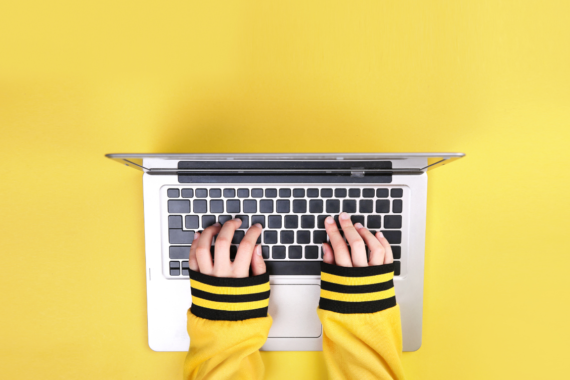 hands typing on computer amongst yellow background