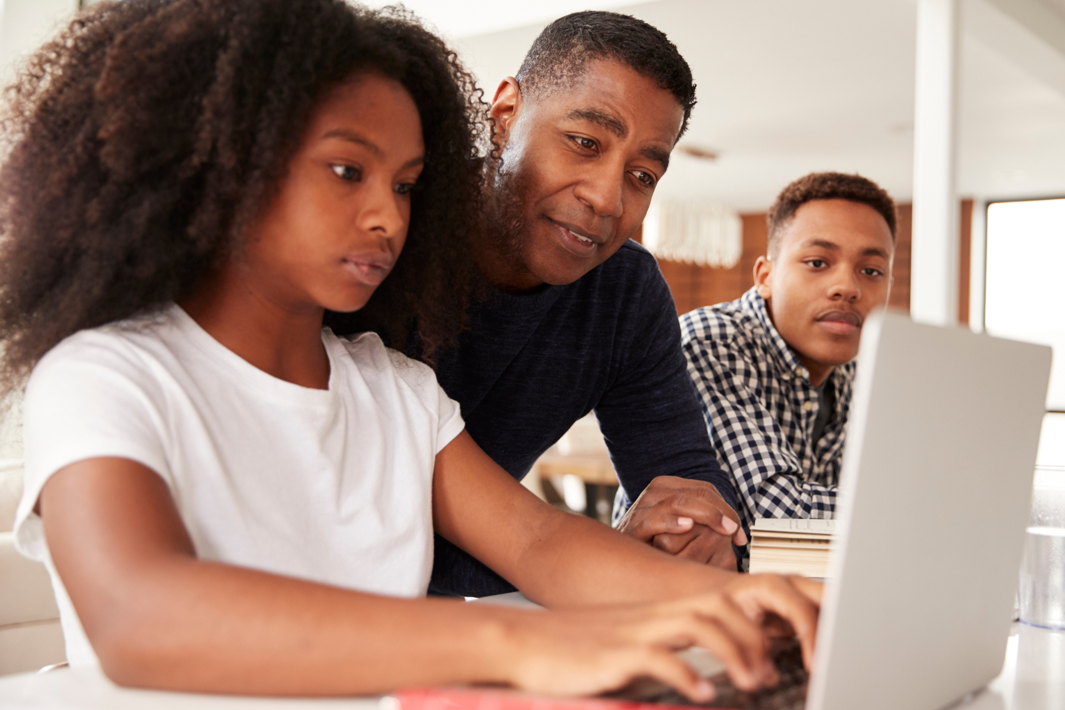 Decorative image of an adult working with two students on a laptop.