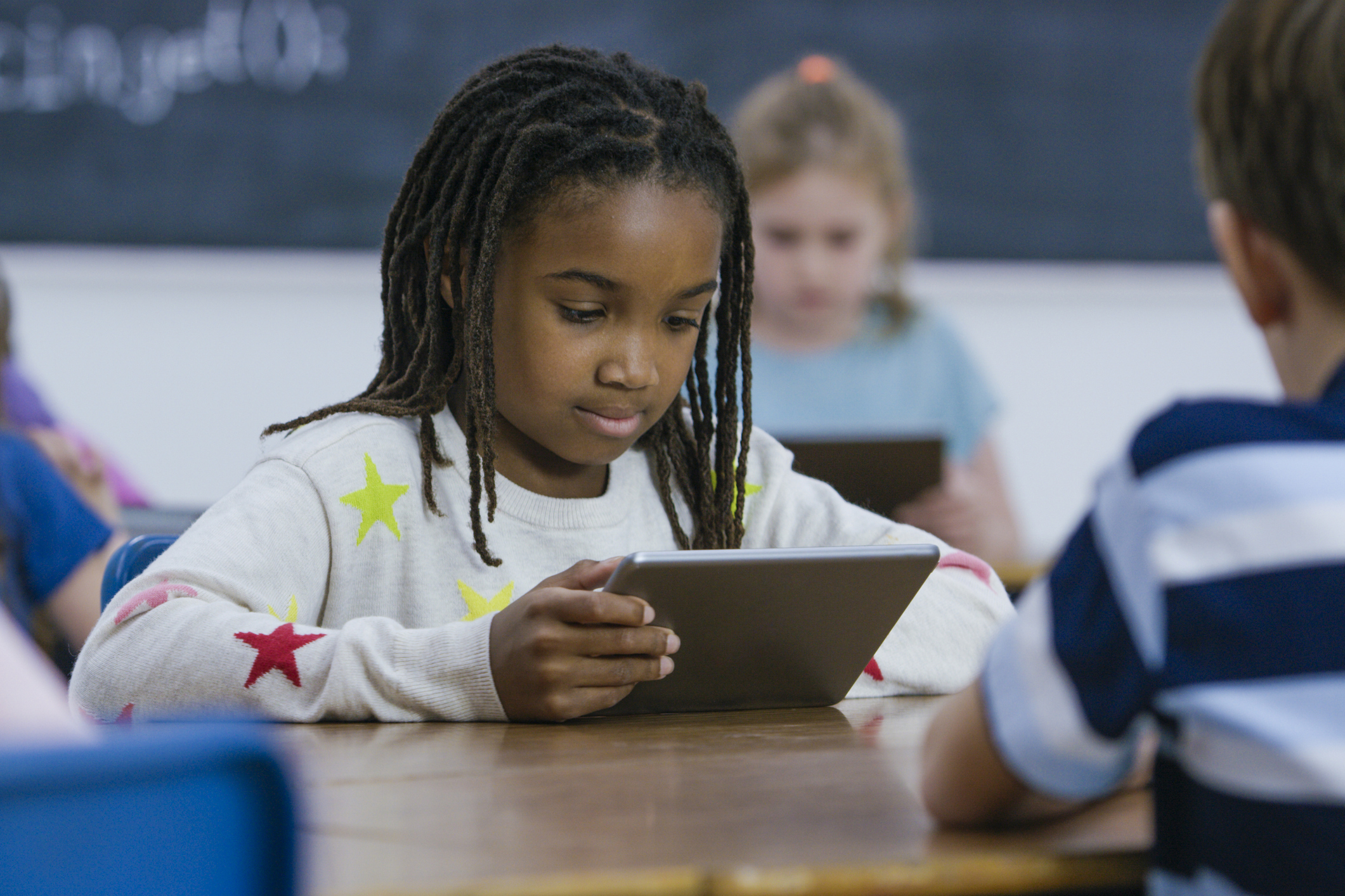 Young girl at a desk in an elementary classroom holding a tablet